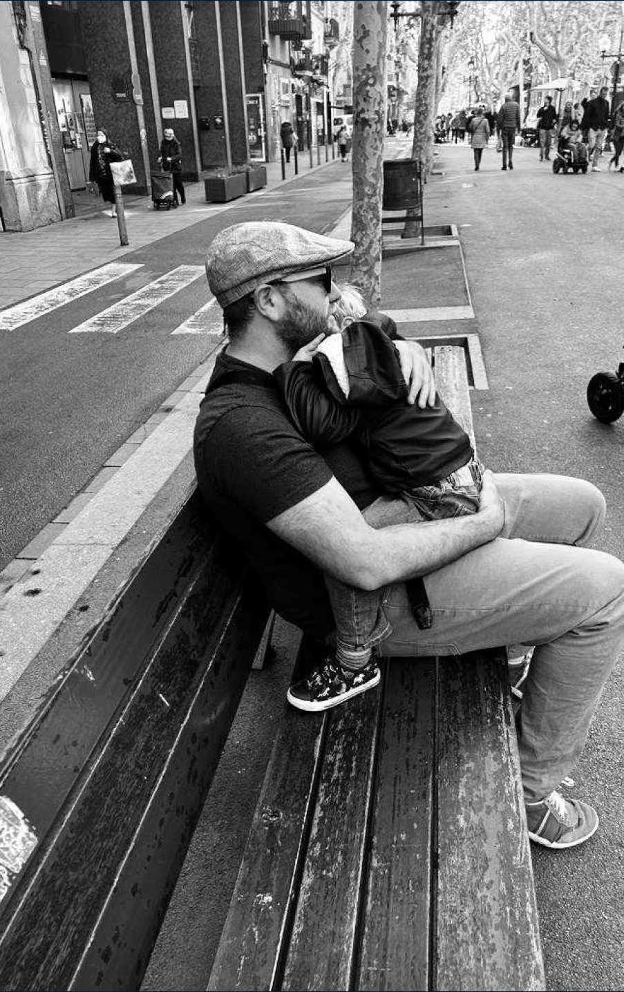 Portrait of Chris holding his child on a city bench.